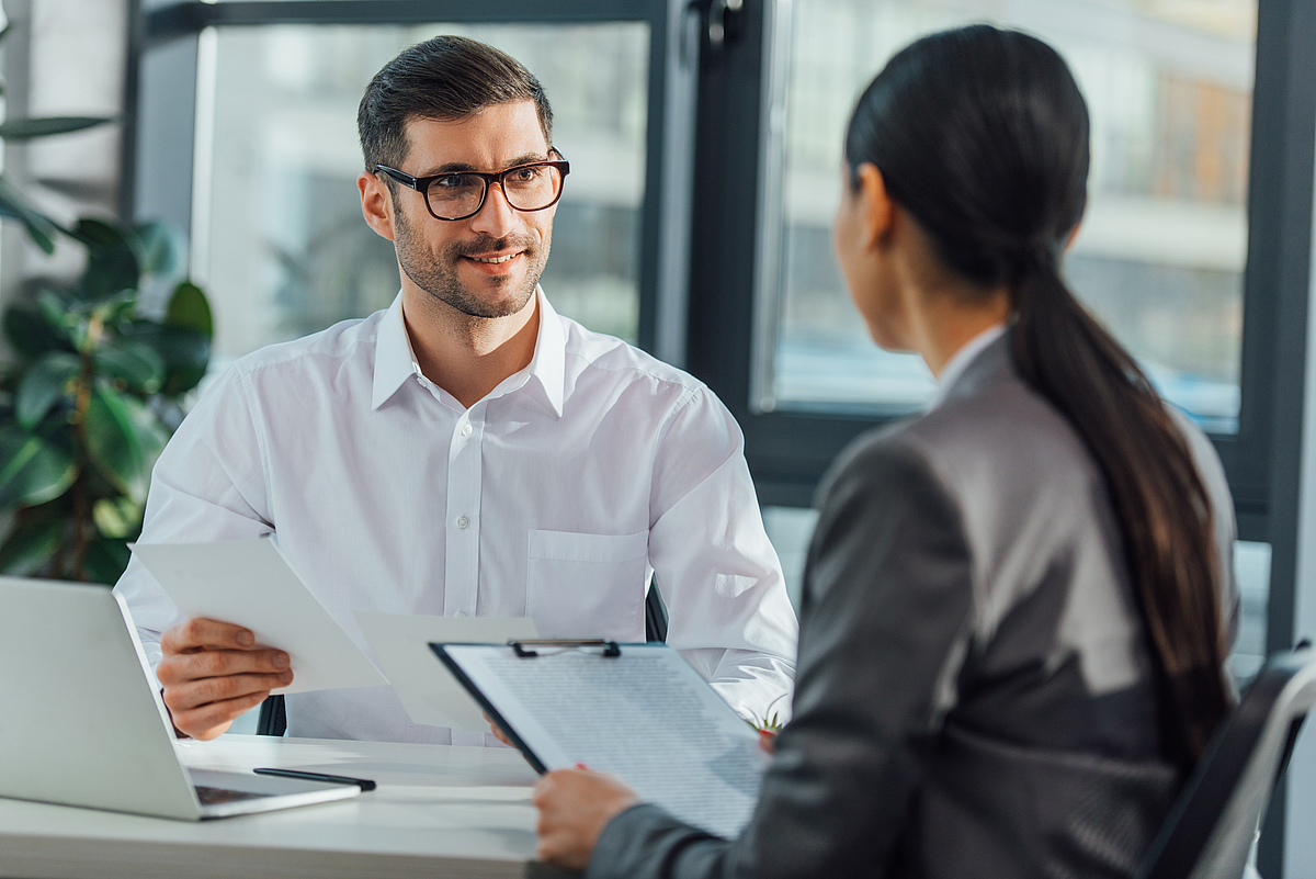 Two translators in a professional office setting, discussing documents across the table.